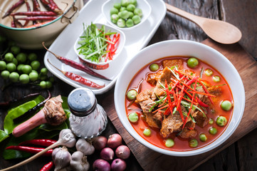 Red curry with pork and coconut milk, delicious Thai food on wooden table.