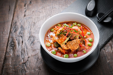Red curry with pork and coconut milk, delicious Thai food on wooden table.