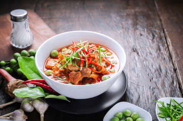 Red curry with pork and coconut milk, delicious Thai food on wooden table.