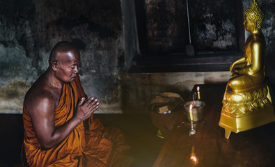 A monk is worshiping and meditating in front of the golden Buddha as part of Buddhist activities.