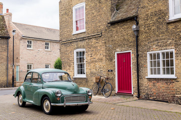 Retro scene with vintage British car 1950 style parked in front of Victorian English building with red door. - 182661593