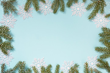 Fototapeta premium Christmas creative border with white snowflakes and branches on blue background. Flat lay. Copy space. Drawn snow.