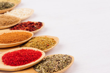 Assortment colorful powdered spices in bamboo spoons, copy space, closeup.