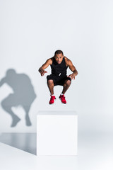 young african american sportsman jumping and looking at camera on grey