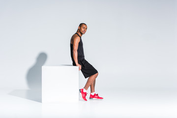 side view of young african american sportsman in sportswear sitting and looking at camera on grey