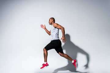 Fototapeta na wymiar side view of young african american sportsman running on grey