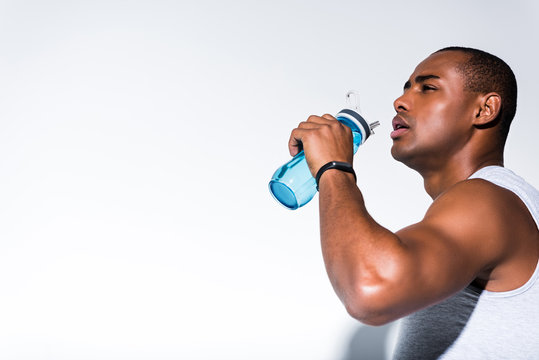 Young African American Sportsman Drinking Water From Sports Bottle On Grey