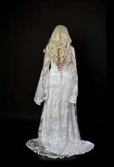 full length portrait of a blonde lady wearing beautiful lace gown, standing pose on black...