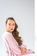 Naklejka premium beautiful girl with makeup sitting on chair and looking away on white