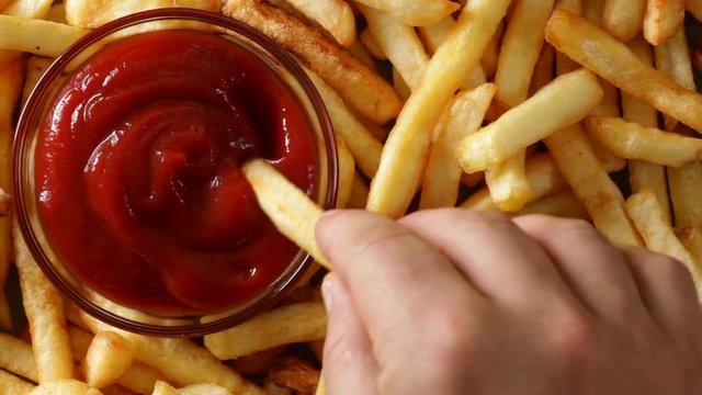 Hands taking french fries and dipping them in ketchup - macro closeup, top view