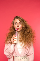surprised girl drinking milkshake with plastic straw isolated on red