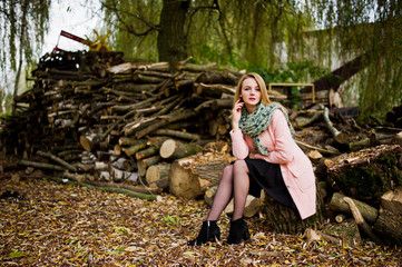 Young blonde girl at pink coat posed against wooden stumps background.