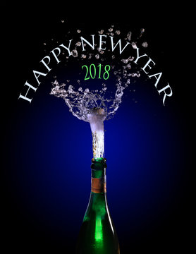 champagne bottle with popping cork and splash against dark blue background, text Happy New Year 2018, motion blur