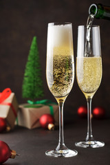 Two champagne glasses for New Year's and Christmas celebration on dark background with gifts and festive toys.