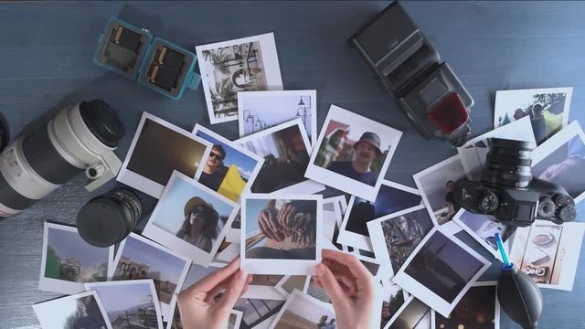 A woman looks at printed photos from travel spread on a wooden table with photo camera and lens.