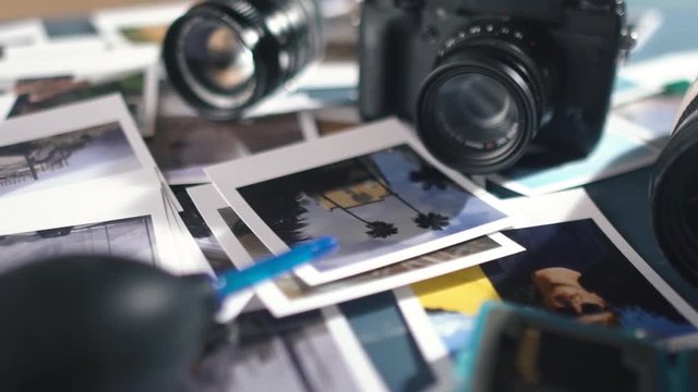 printed photos from travel spread on a wooden table with photo camera and lens