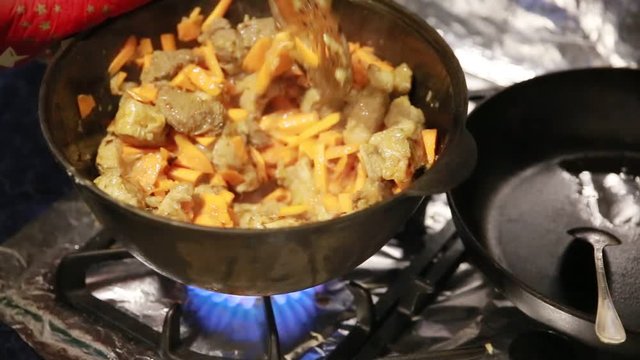 Starting to cook pilaf, shef stirs meat with carrots in a cast-iron kettle