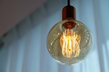 Vintage filament lamp hanging from the ceiling of white curtains background