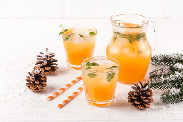 Mandarin cocktail with ice and mint in beautiful glasses and jug, fresh ripe citrus on white wooden background. Sweet orange juice. Close up photography. Selective focus