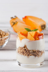 Persimmon creamy trifle in beautiful glasses, fresh ripe fruit slices on white wooden background. Healthy vegetarian food. Delicious dessert. Close up photography. Selective focus.