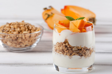 Persimmon creamy trifle in beautiful glasses, fresh ripe fruit slices on white wooden background. Healthy vegetarian food. Delicious dessert. Close up photography. Selective focus.