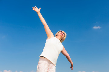 Low-angle view of a fit senior woman looking up to the sky with outstreched arms while enjoying retirement in a sunny day of summer