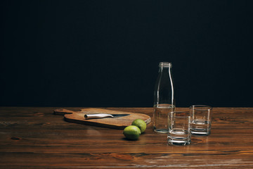 wooden board with knife, limes and water on brown tabletop