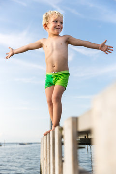 Smiling boy balancing on pier with arm outstretched