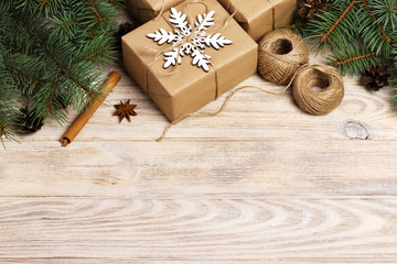 Christmas background with gift boxes wrapped in kraft paper, fir tree branches, pine cones, cinnamon and star anise on white wooden background. Flat lay, top view