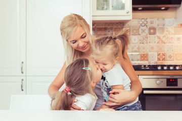 Happy loving young family of mother and her two little daughters. Mother and her children girls playing and hugging at kitchen home