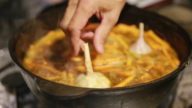 Cooking a pilaf, shef adds garlic into a cast-iron kettle