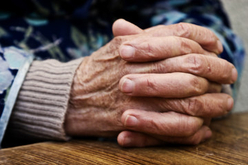 The old grandmother put wrinkled hands on a wooden table