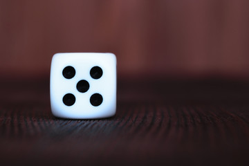 Single white plastic dice on brown wooden board background. Six side cube with black dots. Number 5.