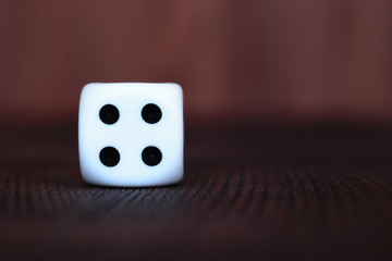 Single white plastic dice on brown wooden board background. Six side cube with black dots. Number 4.