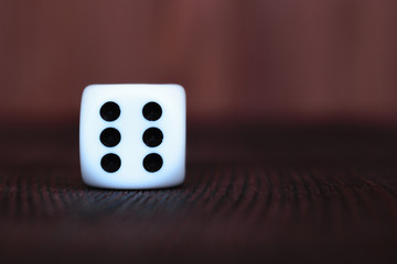 Single white plastic dice on brown wooden board background. Six side cube with black dots. Number 6.
