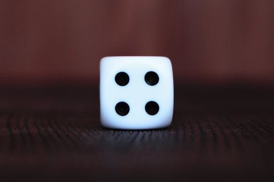 Single white plastic dice on brown wooden board background. Six side cube with black dots. Number four.