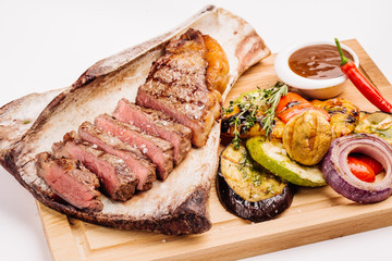 grilled beef steak on the bone with seasonings, fresh rosemary and grilled vegetables on a white background