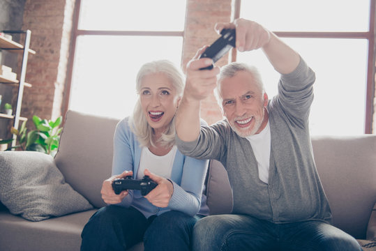 Middle-aged couple excited passionate about car racing game, sitting on a couch in their house in front of the tv screen playing with joysticks, very emotional