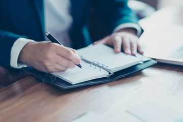 Close up portrait of businessman's hands writing in organizer, planning his week, holding pencil in workplace