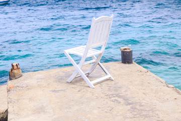 White Wooden Chair on Stone Pier against Azure Sea