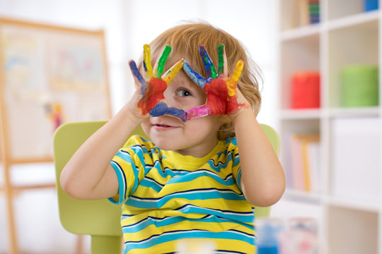 cute cheerful kid boy showing hands painted in bright colors