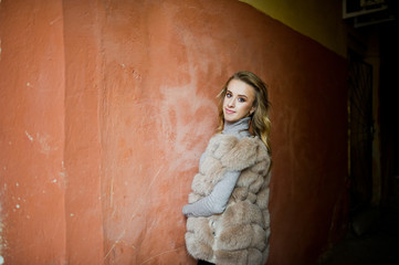 Fototapeta premium Blonde girl at fur coat posed against old orange wall.