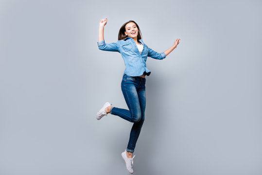 Happiness, freedom, power, motion and people concept - full length portrait of smiling young woman jumping  with raised fists over grey background