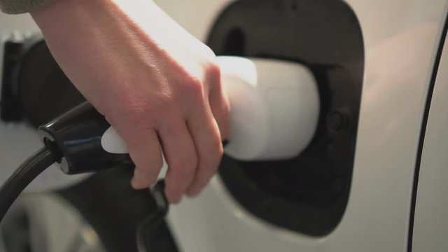 Hand holding electric plug for charging electric car.
