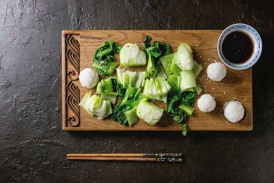 Stir fried bok choy or chinese cabbage with soy sauce and rice balls served on decorative wooden cutting board with chopsticks over dark texture background. Top view with space. Asian style dinner
