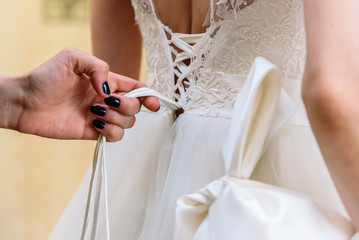 Closeup of bridesmaid tying bow on bride's dress