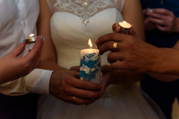 Bride and groom hold white candles in their hands during the ceremony