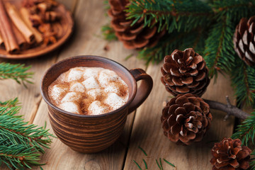 Obraz na płótnie Canvas Spiced hot cocoa with marshmallows on rustic wooden table decorated pine cone and fir tree.