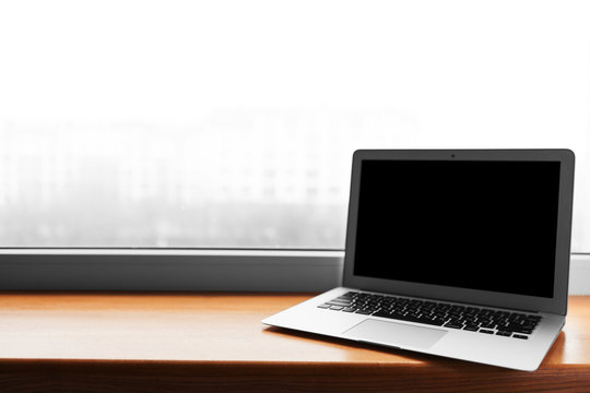 laptop with blank screen on wood table with office window view backgrounds