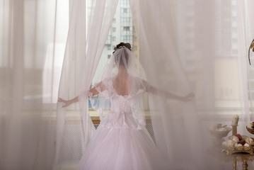 Bride and groom are standing against the window looking outside